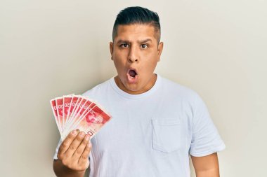Genç latin adam elinde 20 İsrail şekeri tutuyor. Banknotlar korkmuş ve ağzı açık kalmış, şaşırmış ve şaşırmış. 