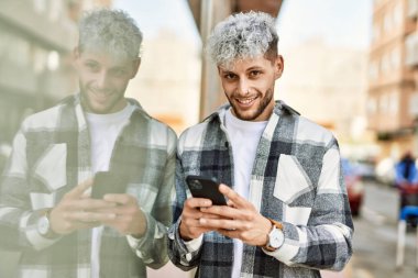Genç İspanyol adam şehirde akıllı telefon kullanarak mutlu gülümsüyor..