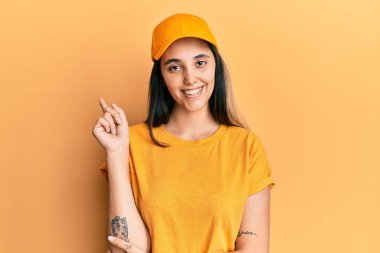 Genç İspanyol kadın teslimat üniforması giyiyor ve yüzünde kocaman bir gülümsemeyle kameraya el ve parmak ile bakıyor.. 