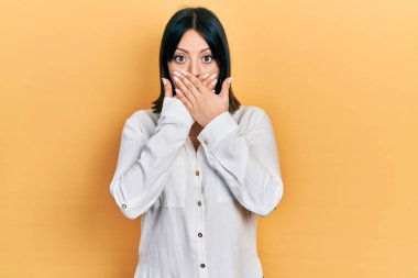 Gündelik kıyafetler giyen genç İspanyol kadın yanlışlıkla elleri ile ağzını kapatırken şok oldu. gizli kavram. 