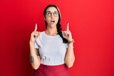 Profesyonel garson önlüğü giyen genç İspanyol kadın şaşırdı ve şaşırdı. Başlarını kaldırıp parmaklarını kaldırdı ve kollarını kaldırdı.. 