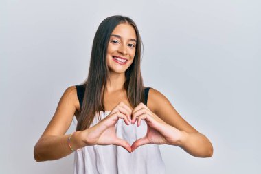 Gündelik giysiler giyen genç İspanyol kadın. Sevgiyle gülümsüyor. Kalp sembolü ve şekli elleriyle gösteriyor. romantik kavram. 