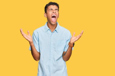 Genç, yakışıklı, Afro-Amerikalı sıradan kıyafetler giyen çılgın ve kızgın bir adam agresif bir ifadeyle bağırıyor ve kollarını kaldırıyor. hüsran kavramı. 