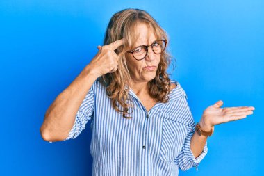 Orta yaşlı, sıradan kıyafetler giyen, gözlüklü bir kadın. Avuç içi boşluğundan rahatsız ve kafası karışık. Kopya alanını gösteren ve alnını işaret eden bir kadın. Bunu bir düşün.. 