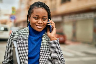 Genç afro-amerikan iş kadını gülümseyerek şehirdeki akıllı telefondan konuşuyor..