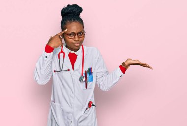 Doktor üniforması giyen genç Afrikalı Amerikalı kadın ve steteskop kafası karışmış ve avuç içi açık bir şekilde fotokopi alanı göstermekten rahatsız olmuş ve alnını işaret ediyor. Bunu bir düşün.. 
