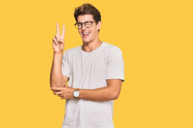 Sıradan kıyafetler ve gözlük takan yakışıklı beyaz adam kameraya gülümseyen gülen yüzle parmaklarıyla zafer işareti yapıyor. İki numara.. 