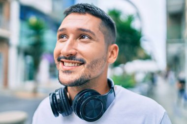 Genç İspanyol adam gülümsüyor. Mutlu bir şekilde müzik dinliyor. Şehir caddesinde kulaklık kullanıyor..