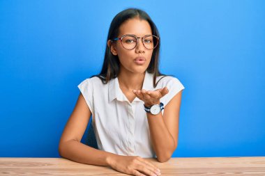 Güzel İspanyol kadın, gündelik giysiler içinde masaya oturmuş kameraya bakıyor ve havada bir öpücük savuruyor. Güzel ve seksi. aşk ifadesi. 