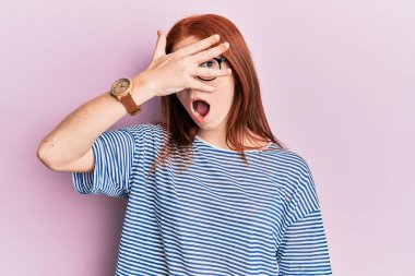 Genç kızıl saçlı kız gündelik kıyafetler ve gözlük takıyor. Şoka girip yüzünü ve gözlerini eliyle kapatıyor. Parmaklarından bakıyor. 