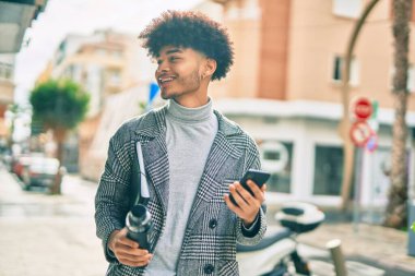 Genç Afrikalı Amerikalı iş adamı şehirde akıllı telefon kullanarak su tutuyor..
