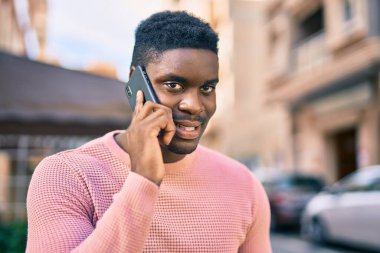 Genç Afrikalı Amerikalı gülümseyen mutlu bir adam şehirdeki akıllı telefondan konuşuyor..