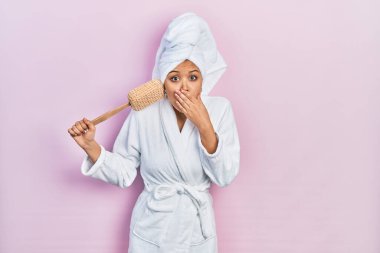 Bornoz giyen genç İspanyol kız elinde süngerle ağzını eliyle kapatıyor, şokta ve hata yapmaktan korkuyor. şaşırmış ifade 