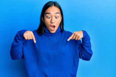 Sıradan bir kazak giyen genç Asyalı kadın parmaklarını göstererek reklamını yapıyor, şaşırmış yüzünü ve ağzını açıyor. 