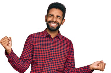 Genç Afro-Amerikan erkeği, gündelik giysiler içinde çok mutlu ve heyecanlı bir şekilde kolları havada, gülümseyerek ve başarı için çığlık atarak kazanan bir jest yapıyor. kutlama konsepti. 