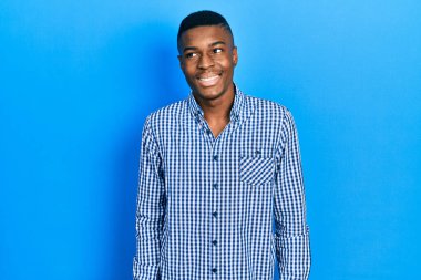 Genç Afro-Amerikan bir adam günlük kıyafetler giyip yüzünde gülümseme, doğal bir ifade ile yan yana bakıyor. Kendinden emin gülen. 