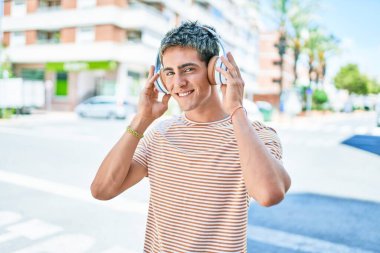 Genç, yakışıklı, beyaz, gülümseyen, müzik dinleyen, kulaklık takan, şehirde yürüyen bir adam..