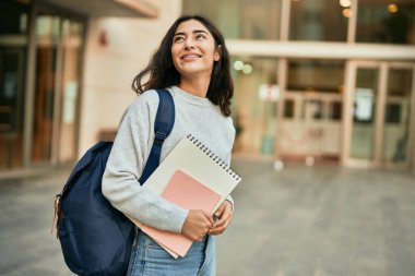 Genç ortadoğulu kız gülümseyerek şehirde mutlu bir kitap tutuyor..