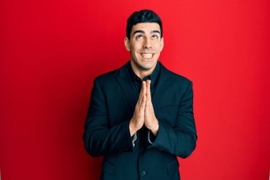 İş kıyafetleri giymiş yakışıklı İspanyol bir adam. Elleriyle yalvarıyor ve dua ediyor. Yüzünde umut ifadesi var. Yalvarıyor. 