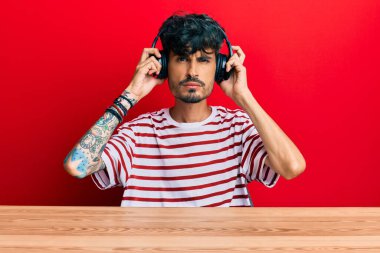 Masada oturan Latin asıllı genç adam şüpheci ve gergin, sorun yüzünden surat asıyor. negatif kişi. 