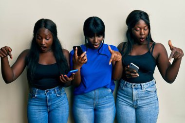 Üç Afro-Amerikalı genç arkadaş akıllı telefon kullanıyor. İlan veren parmaklarıyla işaret ediyorlar. Şaşırmış bir yüz ve açık bir ağız. 