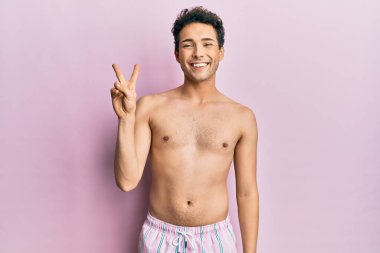 Mayo giyen genç ve yakışıklı bir adam iki numarayı gösterip kendini beğenmiş ve mutlu bir şekilde gülümsüyor.. 