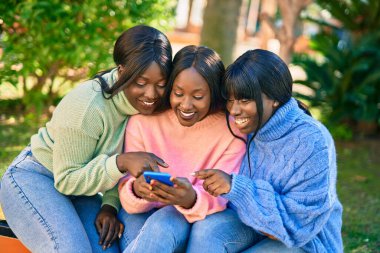 Parkta akıllı telefon kullanarak gülümseyen üç Afrikalı Amerikalı arkadaş..
