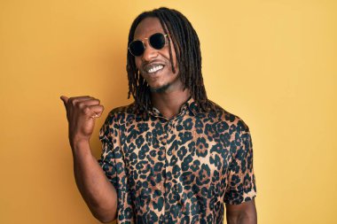 Örgü örgülü, hayvan desenli tişörtlü ve güneş gözlüklü Afro-Amerikan bir adam baş parmağını yana kaldırmış, ağzı açık gülümsüyor. 