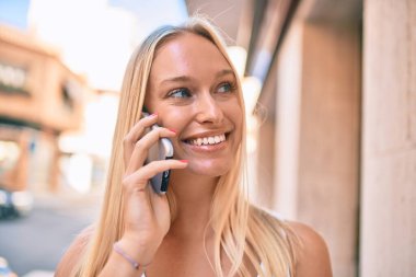Genç sarışın kız gülümsüyor. Şehirdeki akıllı telefondan konuşuyor..