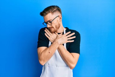 Genç kızıl saçlı profesyonel önlük giymiş mutlu ve olumlu bir şekilde kendine sarılıyor, kendinden emin gülümsüyor. Sevgi ve özgüven. 