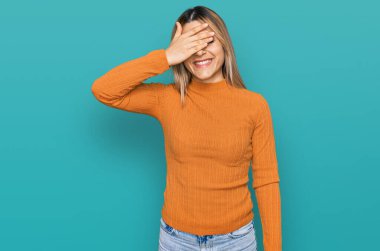 Gündelik giysiler giymiş genç beyaz bir kadın. Gülümsüyor ve elleri yüzüne gülüyor. Şaşırtmak için gözleri örtüyor. kör kavram. 