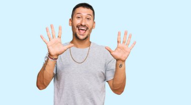 90 'ların tarzında dövmeleri olan yakışıklı bir adam on numarayı gösterip işaret ederken kendinden emin ve mutlu bir şekilde gülümsüyor.. 