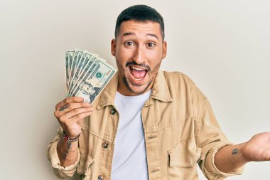 Dövmeleri olan yakışıklı bir adam 20 dolarlık banknotlarla başarıyı kutluyor mutlu bir gülümsemeyle ve kazanan bir ifadeyle elini kaldırarak. 