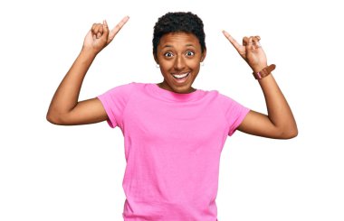 Genç Afrikalı Amerikalı kadın gündelik kıyafetler giyip şaşkın şaşkın gülüyor, parmaklarıyla işaret ediyor ve kollarını kaldırıyordu.. 