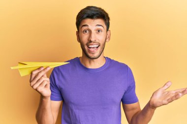 Elinde kağıt uçak tutan genç yakışıklı adam başarıyı mutlu bir gülümsemeyle ve kazanan yüz ifadesiyle kutluyor. 