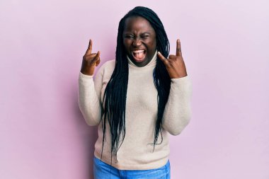 Örgülü, kışlık süveter giyen, çılgın bir ifadeyle bağıran, elleri havada rock sembolü yapan genç siyahi bir kadın. Müzik yıldızı. ağır kavram. 