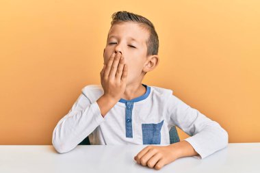 Kafkasyalı sevimli bir çocuk, gündelik giysiler giyip masada oturmaktan sıkılmış, ağzı eliyle kapatmaktan bıkmış. Huzursuz ve uykulu.. 