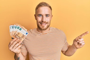 Elinde 50 avroluk banknotlar tutan beyaz bir adam gülümsüyor. 