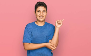 Gündelik kıyafetler giyen, yüzünde kocaman bir gülümseme olan, eli ve parmağı kameraya bakan genç İspanyol çocuk.. 