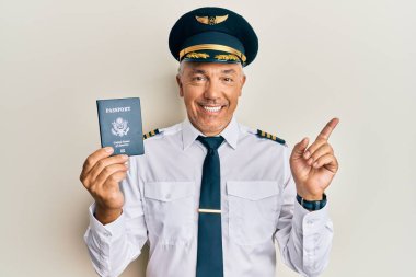 Yakışıklı, orta yaşlı, olgun bir pilot. Elinde pasaportuyla gülümsüyor. Elini ve parmağını yana uzatarak mutlu bir şekilde işaret ediyor. 