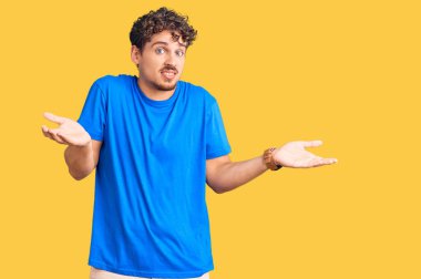 Kıvırcık saçlı, sıradan kıyafetler giyen, kafası karışık ve kolları açık genç bir adam.. 