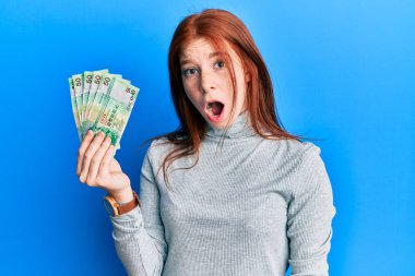 Genç kızıl saçlı kız 50 Hong Kong doları tutuyor. Banknotlar korkmuş ve hayrete düşmüş. 