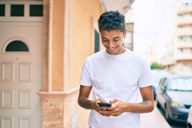 Genç Latin adam mutlu bir şekilde gülümsüyor ve şehirde akıllı telefon kullanıyor..
