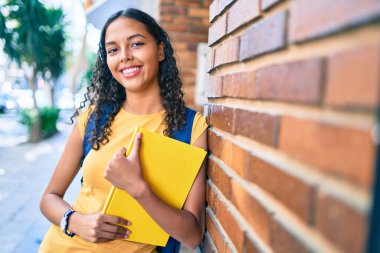Genç Afrikalı Amerikalı öğrenci üniversite kampüsünde mutlu bir şekilde kitap tutuyor..