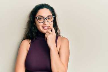 Gündelik kıyafetler ve gözlük takan güzel bir orta doğulu kadın kameraya kolları çapraz ve çenesi açık bir şekilde bakıyor. Olumlu düşünmek. 