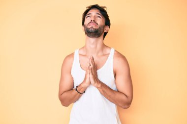 Yaz bakışı ve güneş gözlüğü takan yakışıklı İspanyol adam elleri ile yalvarıyor ve dua ediyor. Yüzünde umut ifadesi var. Çok duygusal ve endişeli. Yalvarıyor. 