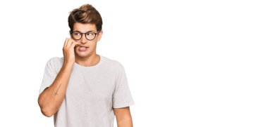 Sıradan kıyafetler ve gözlük takan yakışıklı beyaz adam gergin görünüyor ve elleri ağızdan tırnak yiyor. anksiyete. 