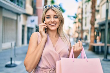 Genç sarışın kadın gülümsüyor. Akıllı telefondan konuşmaktan mutlu oluyor. Şehre alışverişe gidiyor..