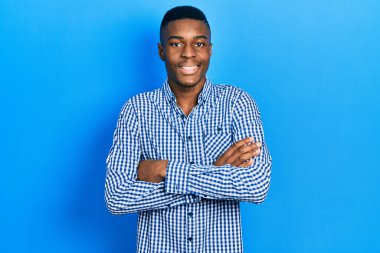 Sıradan kıyafetler giyen, kollarını kavuşturup kameraya gülümseyen Afro-Amerikan genç adam. pozitif kişi. 