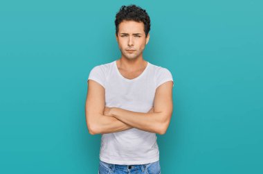 Sıradan beyaz tişört giyen, kuşkucu ve gergin genç yakışıklı bir adam. Yüzünde çapraz kollu tasvip etmeyen bir ifade var. negatif kişi. 